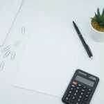 black calculator beside black pen on white printer paper